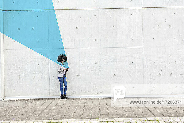 Junge Frau  die im Freien steht und ihr Smartphone in den Händen hält  bedeckt mit blauem Gesichtserkennungseffekt