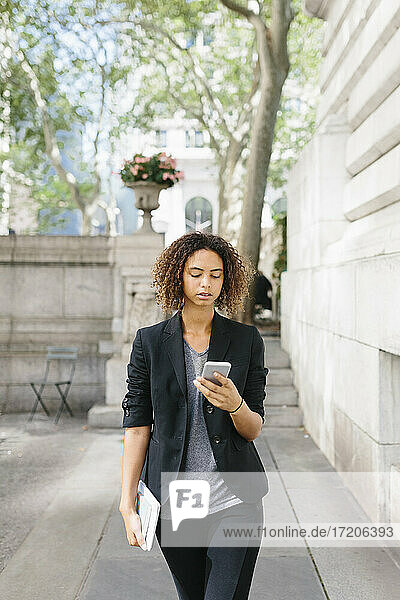 Afro-Geschäftsfrau benutzt Smartphone beim Gehen auf dem Fußweg
