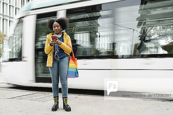 Junge Frau schreibt SMS auf ihrem Handy  während sie auf dem Fußweg vor der Straßenbahn steht