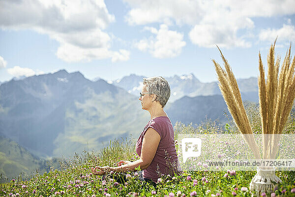 Mature woman meditating amidst plants against sky