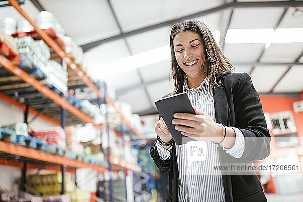 Lächelnde Managerin mit digitalem Tablet in einem beleuchteten Vertriebslager