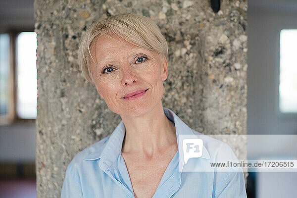 Lächelnde Geschäftsfrau mit blauen Augen an einer Säule zu Hause