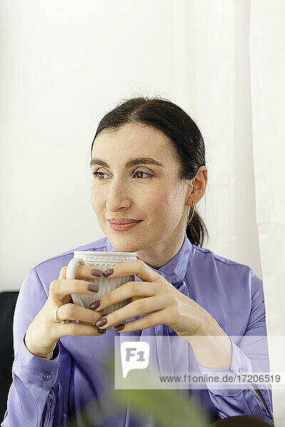Nachdenkliche Geschäftsfrau hält Kaffeebecher zu Hause