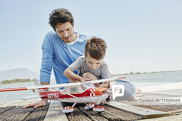 Junge prüft Spielzeugflugzeug  während er auf dem Pier sitzt