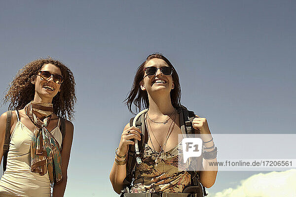 Lächelnde Freundinnen stehen gegen den Himmel während des Wochenendes