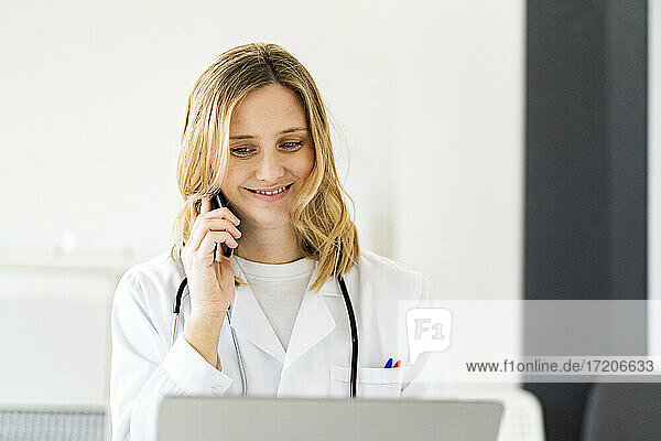 Lächelnde blonde Ärztin  die mit einem Smartphone in einer medizinischen Klinik spricht