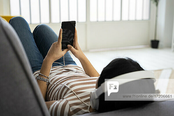 Relaxed young woman listening music through wireless headphones while lying on sofa at home