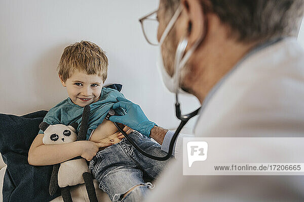 Kinderarzt  der einen lächelnden Jungen mit Stethoskop in einer Klinik untersucht