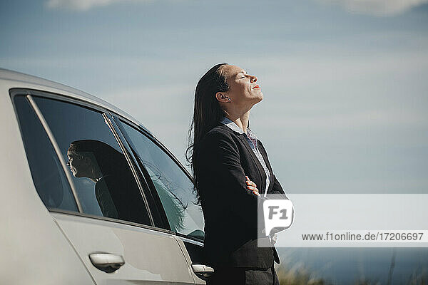 Nachdenkliche Geschäftsfrau  die mit geschlossenen Augen und verschränkten Armen neben einem Auto steht