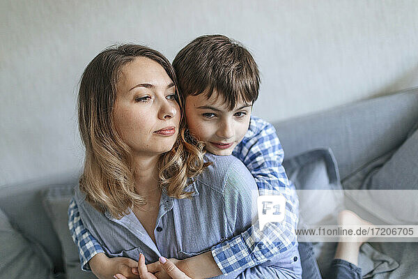 Son looking away while embracing mother at home