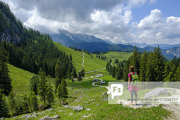 Wanderin steht mitten auf einem Wanderweg  der sich durch ein Sommertal in den Berchtesgadener Alpen schlängelt