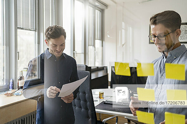 Male colleagues seen through glass while discussing in office
