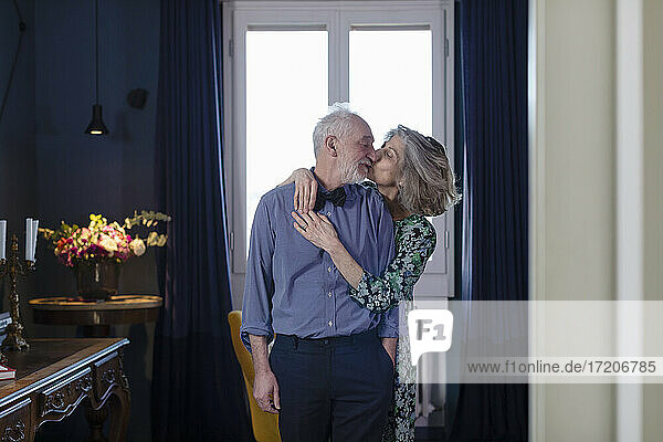Senior woman kissing man while standing at home