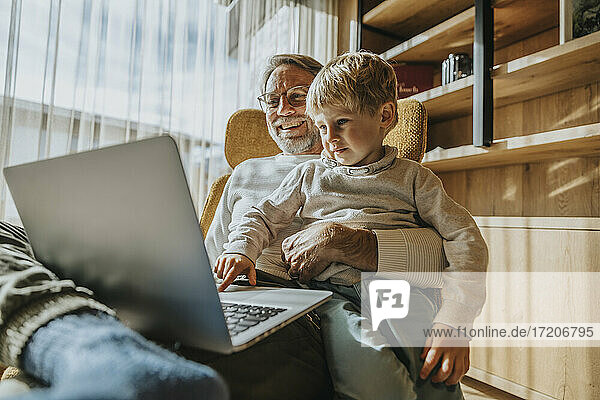 Junge benutzt Laptop  während er mit seinem Vater auf einem Stuhl sitzt