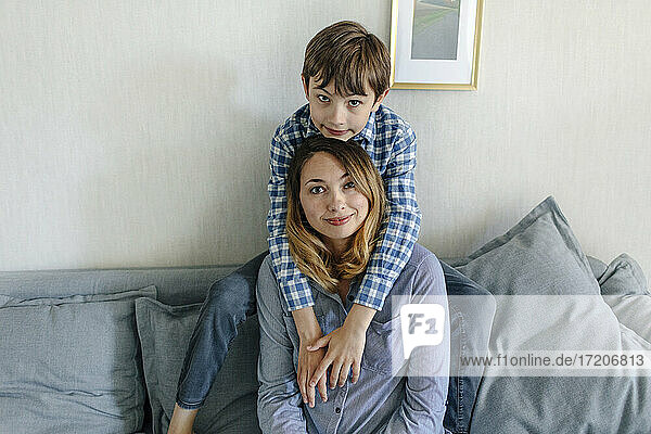 Junge umarmt Mutter von hinten auf dem Sofa