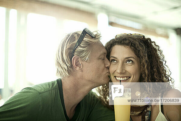 Junger Mann küsst lächelnd eine Frau  während er im Café sitzt