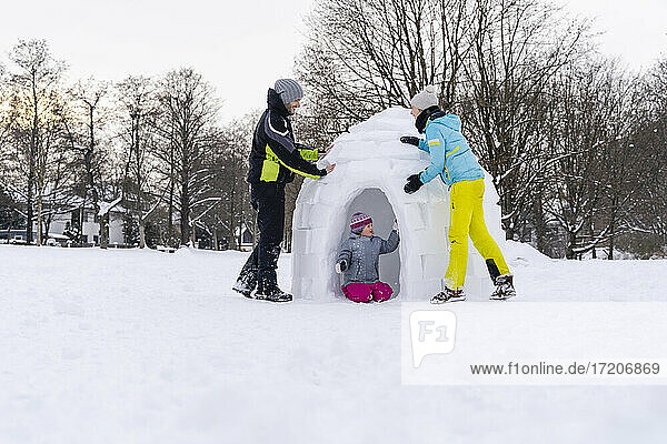 Vater und Mutter helfen ihrer Tochter beim Bau eines Iglus im Schnee im Park