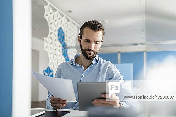 Männlicher Berufstätiger mit Papier und digitalem Tablet im Büro sitzend