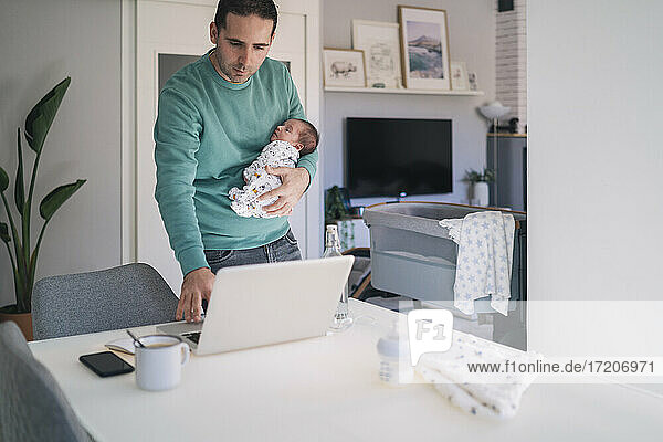 Geschäftsmann  der einen kleinen Jungen trägt  während er im Büro zu Hause am Laptop arbeitet