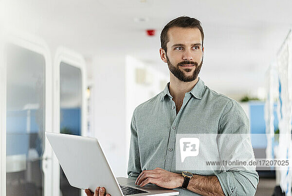 Junge männliche Fachkraft mit Laptop im Büro stehend