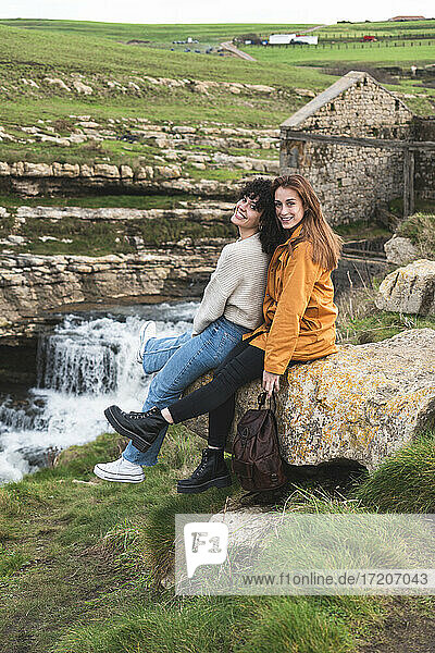 Glückliche Freundinnen sitzen auf einem Felsen am Wasserfall