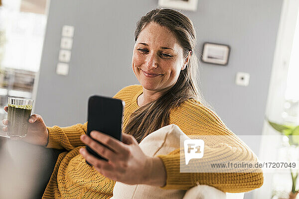Glückliche erwachsene Frau  die ein Mobiltelefon im Wohnzimmer benutzt