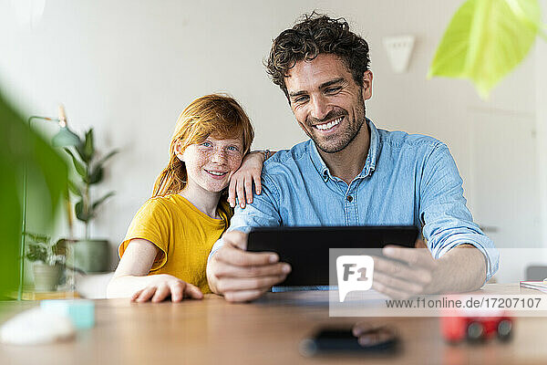 Lächelnder Vater schaut auf ein digitales Tablet  während er bei seiner Tochter zu Hause sitzt