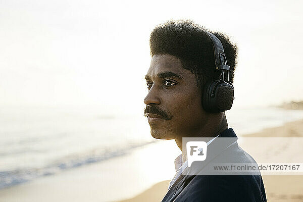 Nachdenklicher Afro-Mann mit Kopfhörern am Strand