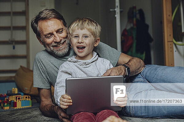 Lächelnder Vater und Sohn verwenden Tablet im Schlafzimmer