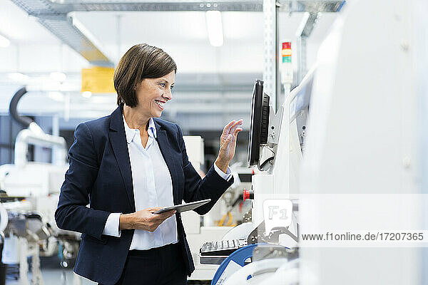 Happy businesswoman with digital tablet operating machinery in factory