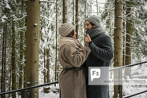 Girlfriend and boyfriend looking at each other while standing with hands clasped in forest