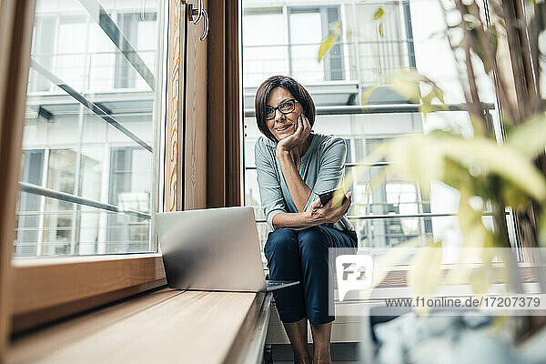 Unternehmerin mit Smartphone  die wegschaut  während sie im Büro sitzt