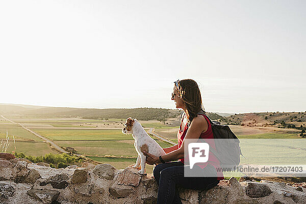 Lächelnde Frau  die einen Hund hält und auf einem Felsen gegen den Himmel sitzt