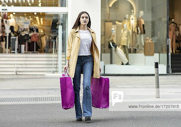 Junge Frau geht mit magentafarbenen Einkaufstaschen vor einem Geschäft