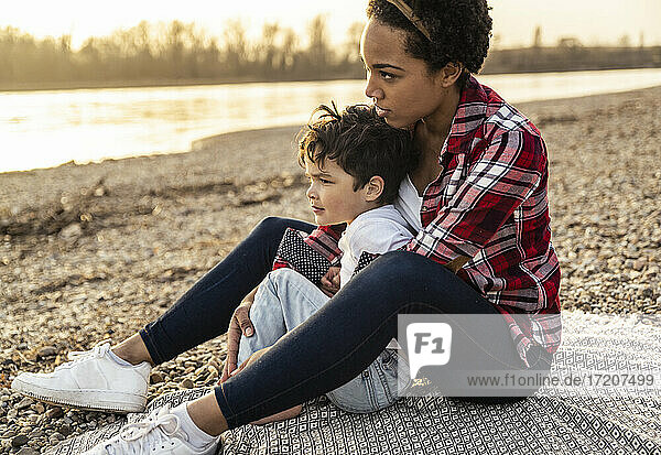 Young woman sitting with arm around on boy during sunset