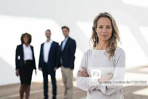 Selbstbewusste Geschäftsfrau  die auf einer Büroterrasse mit Kollegen im Hintergrund steht und starrt