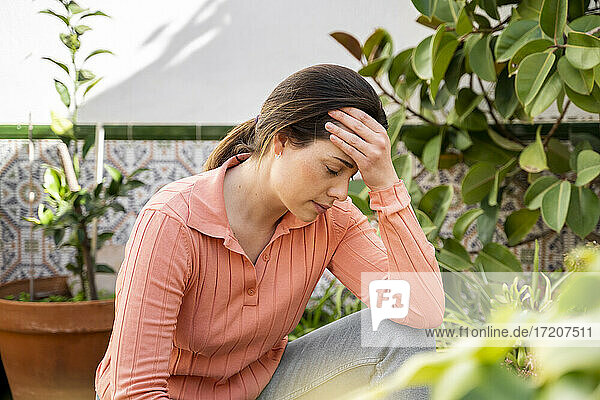 Tensed young woman with head in hand sitting in garden