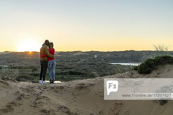 Junges Paar mit Blick auf den Sonnenuntergang auf einer Sanddüne stehend