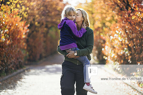 Mother kissing while carrying daughter in park
