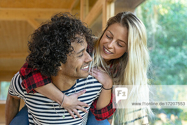 Smiling man piggybacking woman while standing by window at front yard
