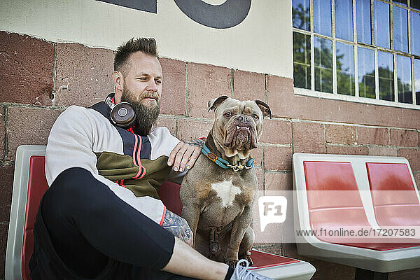 Männlicher Fitnesstrainer  der eine Bulldogge betrachtet  während er vor einem Fitnessstudio sitzt