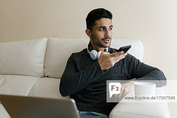 Young man talking through smart phone while sitting on sofa at home