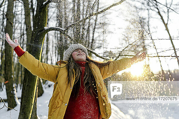 Mädchen in warmer Kleidung steht mit geschlossenen Augen unter einem Baum bei Schneefall
