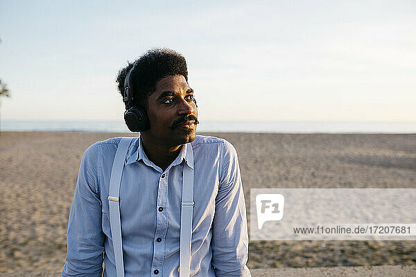 Afro-Mann träumt am Strand und hört Musik über Kopfhörer gegen den klaren Himmel
