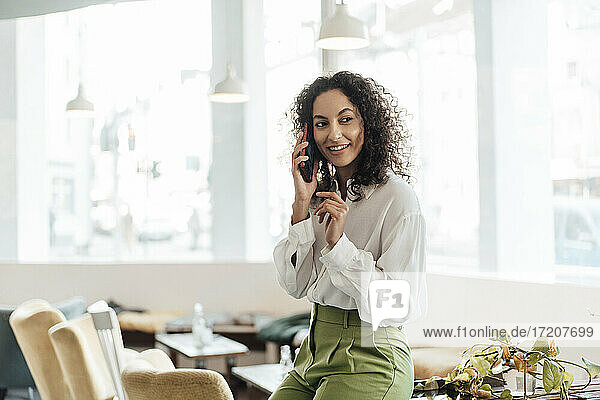 Young businesswoman talking on mobile phone while sitting on table at cafe
