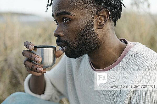 Junger Mann trinkt Tee am Strand