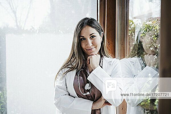 Smiling female doctor with hand on chin leaning on window