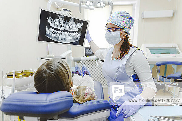 Eine Zahnärztin zeigt einem kleinen Mädchen  das im Zahnarztstuhl liegt  ein Röntgenbild