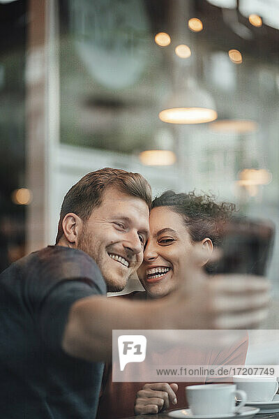 Glückliches Paar nimmt Selfie durch Handy beim Sitzen im Café