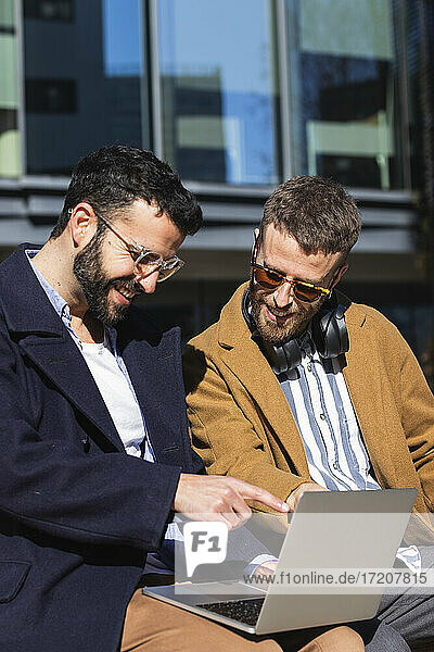 Lächelnde Geschäftsleute  die im Freien sitzend am Laptop arbeiten